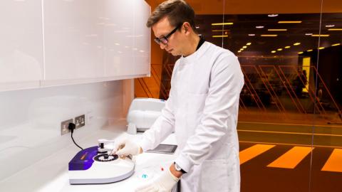 A man in a white coat stands in a lab